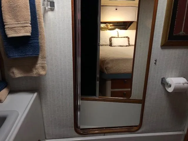 Slide: The Image of 1988 Bayliner 3818 Motoryacht bathroom with mirror, towels, and visible bedroom reflection. - 49