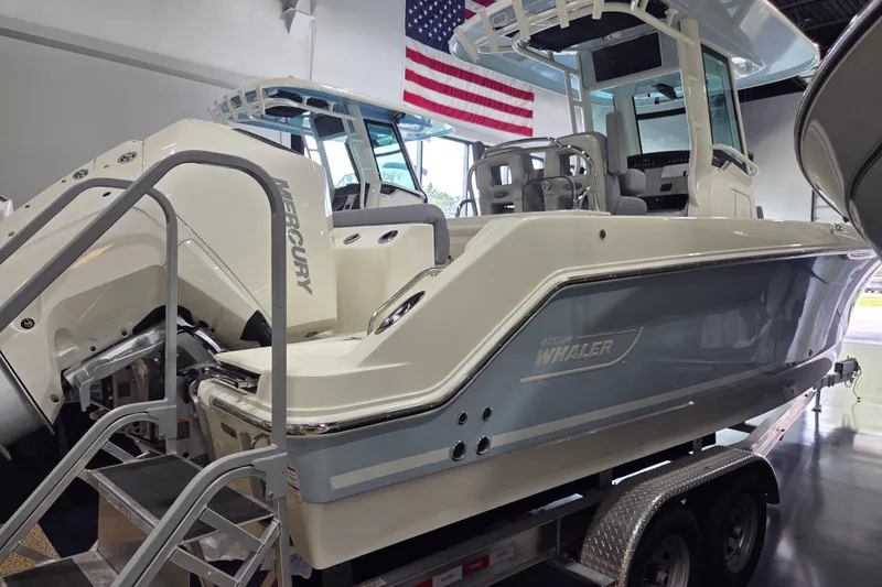 Slide: The Image of 2025 Boston Whaler 250 Outrage boat on trailer, displayed indoors with American flag. - 5