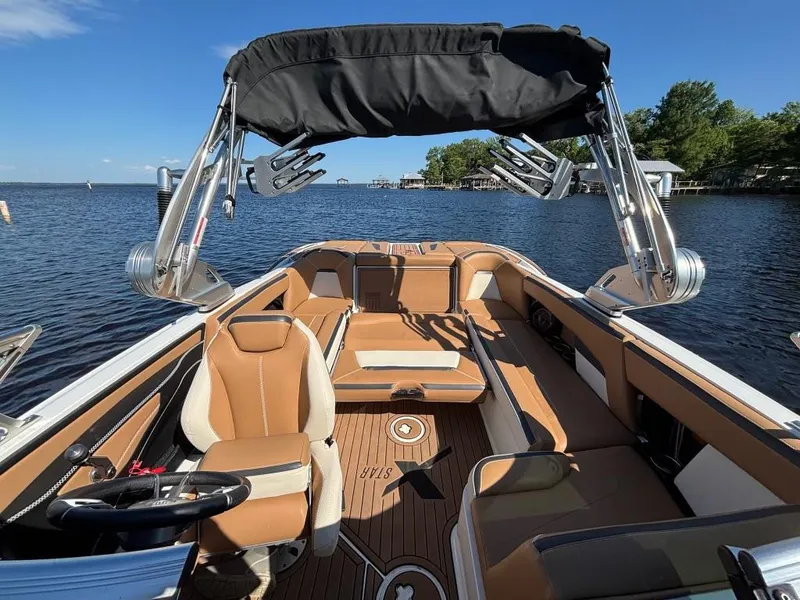 Slide: The Image of 2019 MasterCraft XStar boat interior with tan seating and black canopy on a sunny lake. - 13