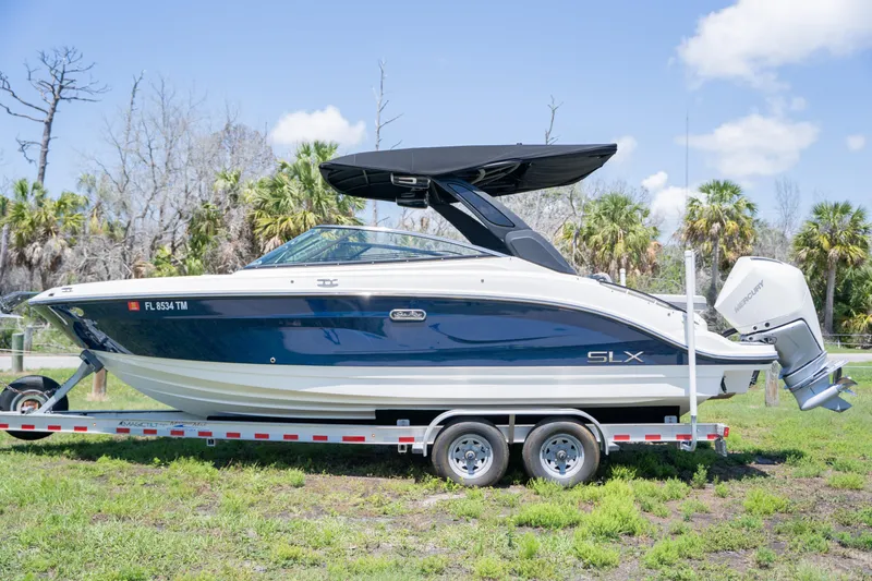Slide: The Image of 2023 Sea Ray SLX 260 Outboard boat on trailer, parked on grass, under clear sky. - 2