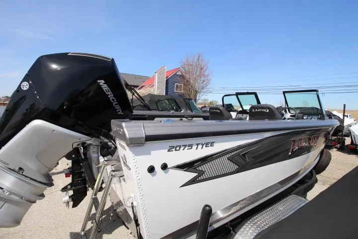 Slide: The Image of 2025 Lund 2075 Tyee boat with Mercury engine, parked outdoors under clear blue sky. - 1