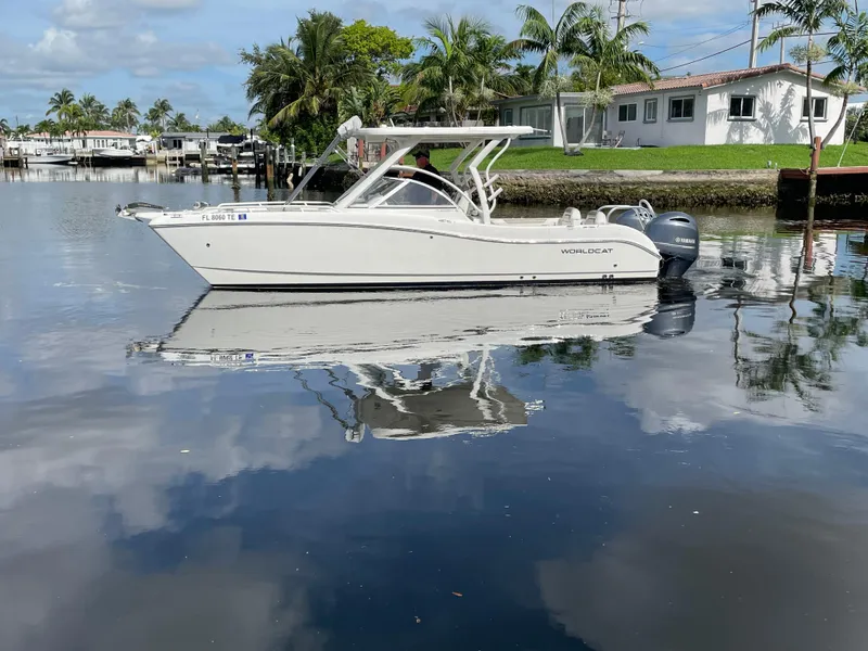 Slide: The Image of 2022 World Cat 255 DC boat on calm water with palm trees and houses in the background. - 7