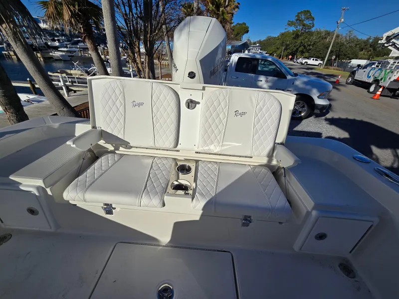 Slide: The Image of 2025 Ranger 2360 Bay boat with white cushioned seating and motor, parked near marina. - 15