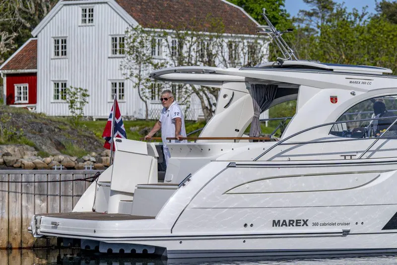 Slide: The Image of 2025 Marex 360 Cabriolet Cruiser docked near a white house, with a person on board. - 31