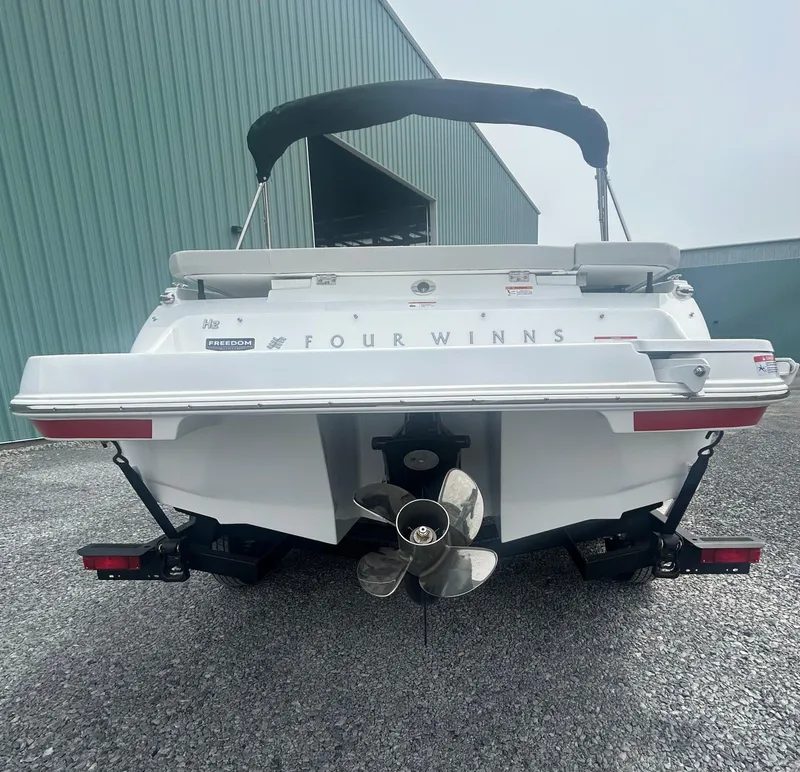 Slide: The Image of 2025 Four Winns H2 Freedom boat rear view with propeller, parked on gravel. - 5
