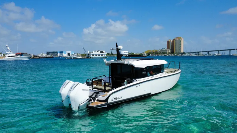 Slide: The Image of 2024 XO Boats EXPLR 10S Plus cruising in clear blue waters near a cityscape. - 2