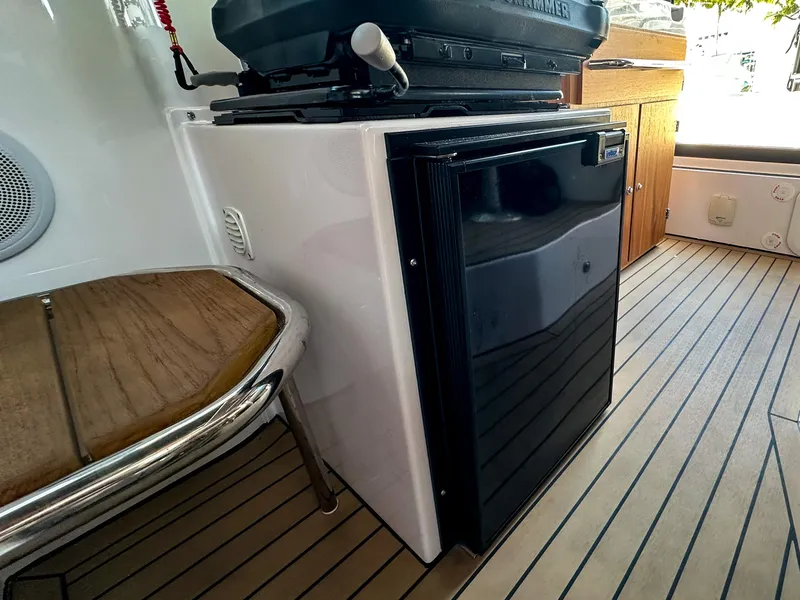 Slide: The Image of 2024 XO Boats EXPLR 10 Sport Plus interior with compact fridge and wooden flooring. - 29