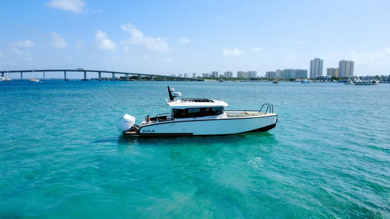 Slide: The Image of 2024 XO Boats EXPLR 10S Plus cruising in clear blue waters near a cityscape. - 34