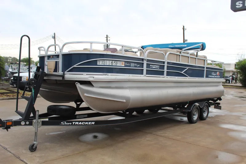 Slide: The Image of 2019 Sun Tracker Fishin' Barge 22 DLX pontoon boat on trailer, parked outdoors. - 3