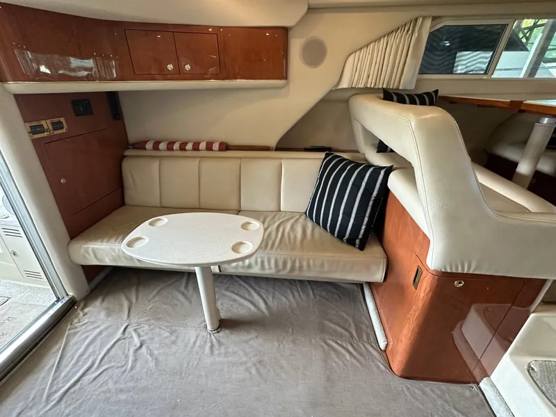Slide: The Image of 1999 Sea Ray 400 Sedanbridge interior with beige seating, striped pillows, and a small round table. - 11
