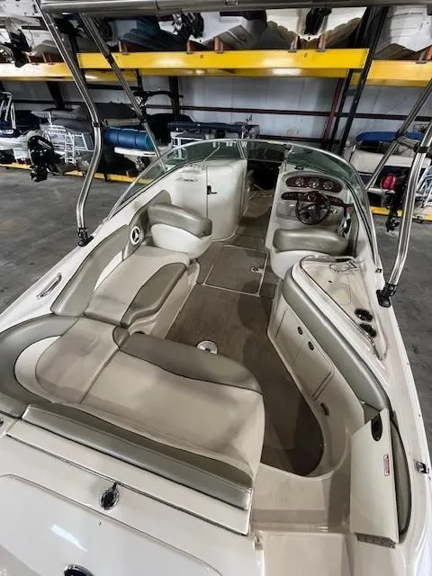 Slide: The Image of 2006 Sea Ray Sundeck 240 interior with beige seating and dashboard, stored indoors. - 10