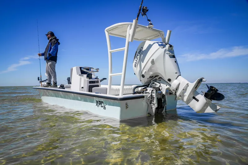 Slide: The Image of Man fishing on Custom XPC 16 boat, 2025 model, in shallow waters under clear blue sky. - 13