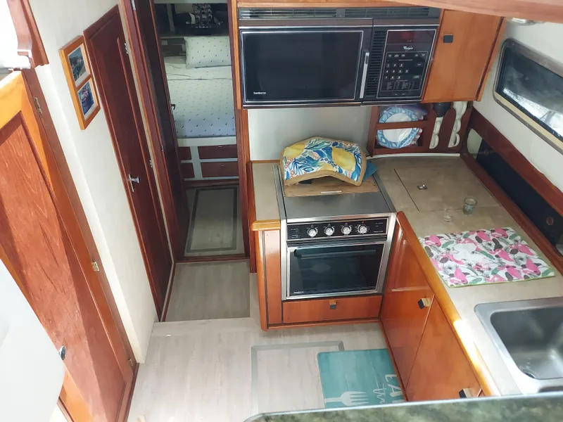 Slide: The Image of 1987 Bayliner 3870 Motoryacht kitchen with stove, microwave, and sink, featuring wood cabinetry. - 10