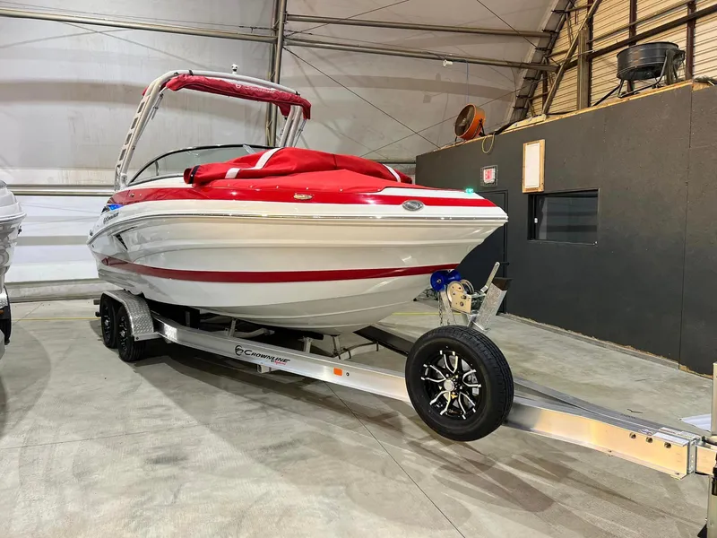 The Image of 2024 Crownline 250XSS boat with red accents on a trailer in a warehouse. - 0