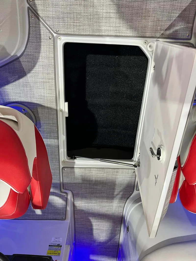 Slide: The Image of 2024 Crownline 250XSS boat interior with open storage compartment and red seating. - 5