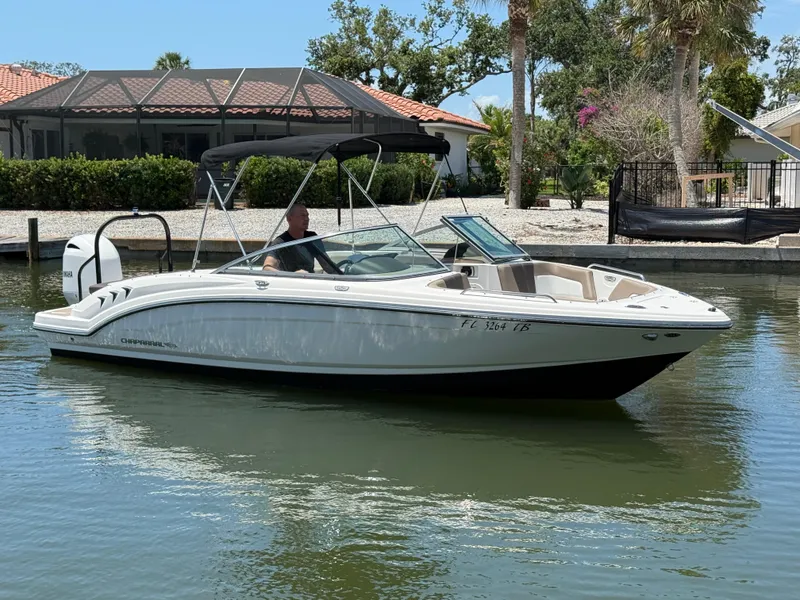 The Image of 2021 Chaparral 23 SSi OB boat cruising on a calm waterway near a residential area. - 1