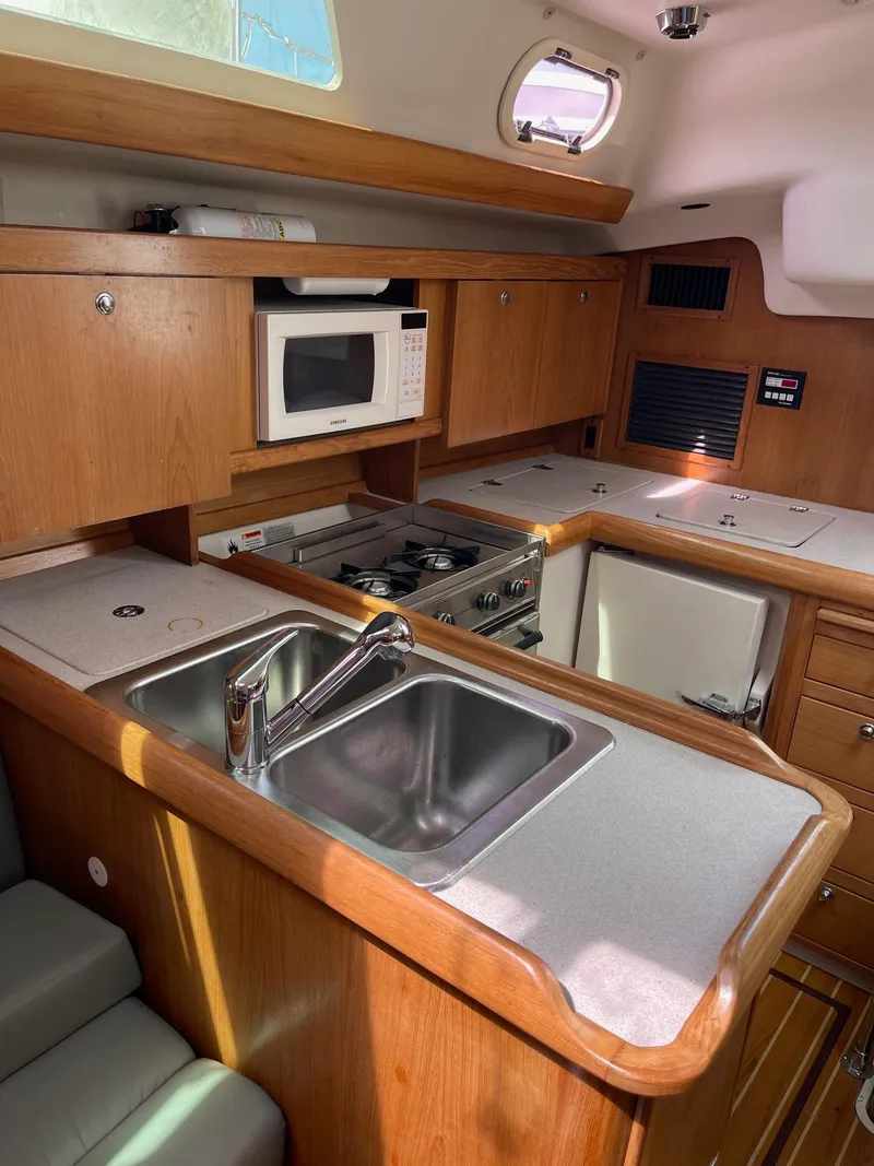 Slide: The Image of 2004 Catalina 350 yacht kitchen with sink, stove, microwave, and wooden cabinetry. - 10