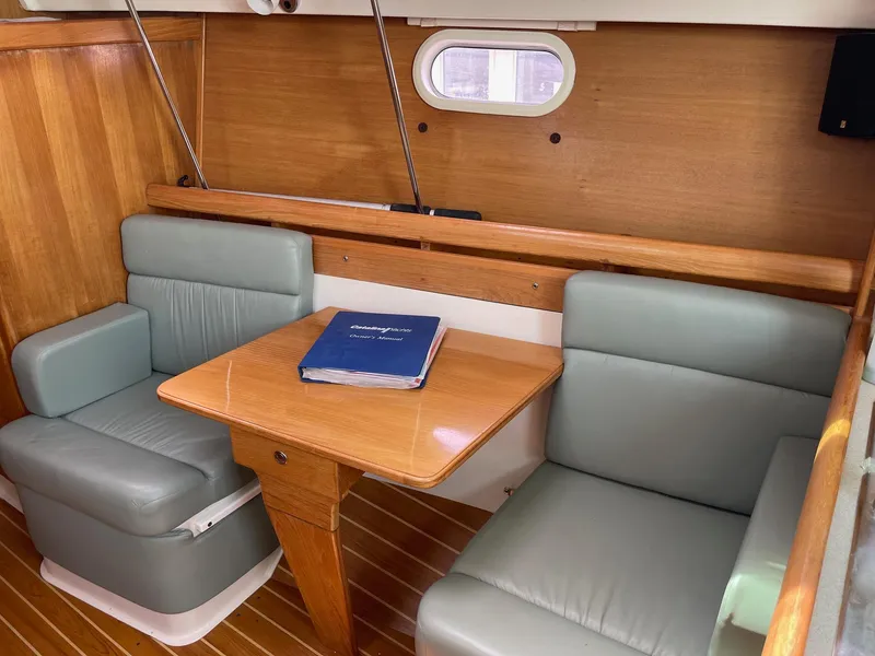 Slide: The Image of 2004 Catalina 350 yacht interior with wooden table, cushioned seating, and a manual on the table. - 12