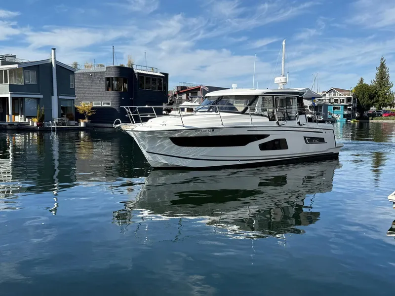 Slide: The Image of 2021 Jeanneau NC Weekender 1095 boat docked on calm water, modern waterfront homes in background. - 25