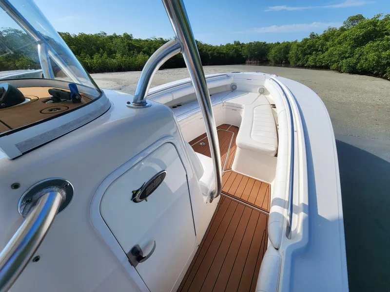 Slide: The Image of 2015 Regulator 25 boat with sleek white design and wooden deck, docked near lush greenery. - 18