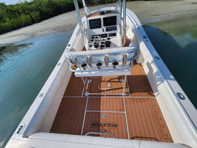 Slide: The Image of 2015 Regulator 25 boat with teak deck, center console, and rod holders near shoreline. - 7