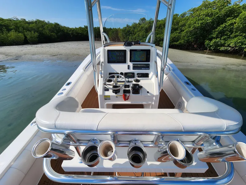 Slide: The Image of 2015 Regulator 25 boat with dual consoles, docked near a sandy shore and lush greenery. - 8