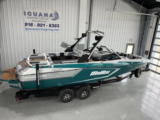 The Image of 2025 Malibu Wakesetter 24 MXZ boat in showroom, teal and white design, on trailer. - 1