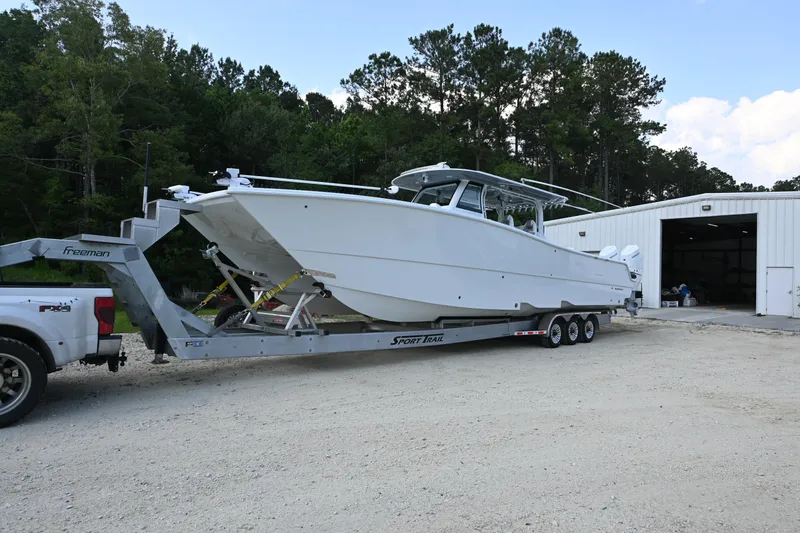 Slide: The Image of 2024 Freeman 43 boat on trailer near a white building, surrounded by trees. - 36