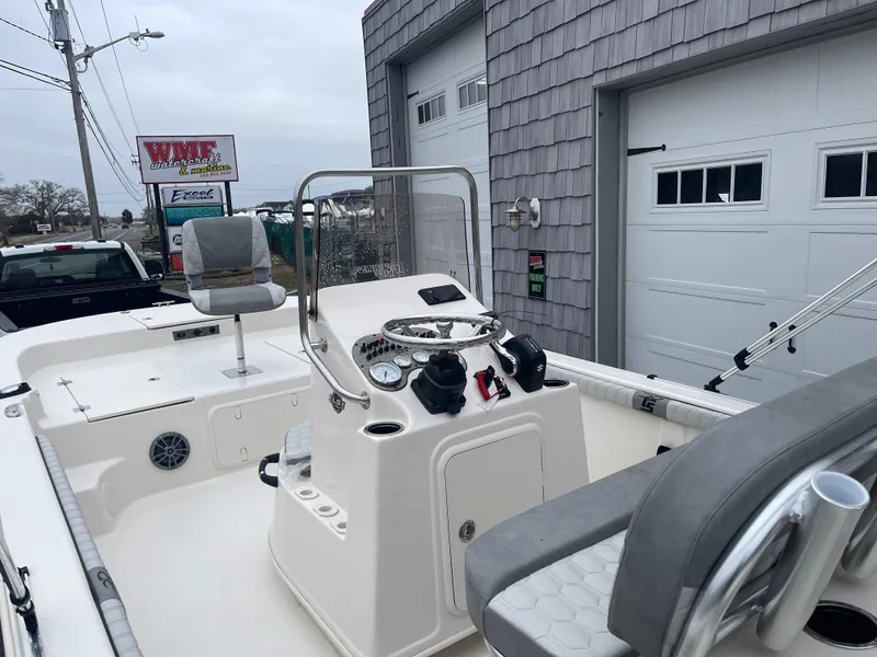 Slide: The Image of 2025 Carolina Skiff 21 LS boat interior with steering console and seating, parked near a garage. - 12