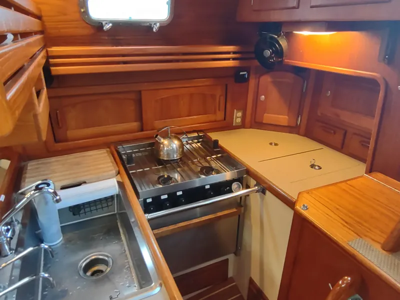 Slide: The Image of Cozy 1997 Pacific Seacraft 37 yacht kitchen with stove, sink, and wooden cabinetry. - 28
