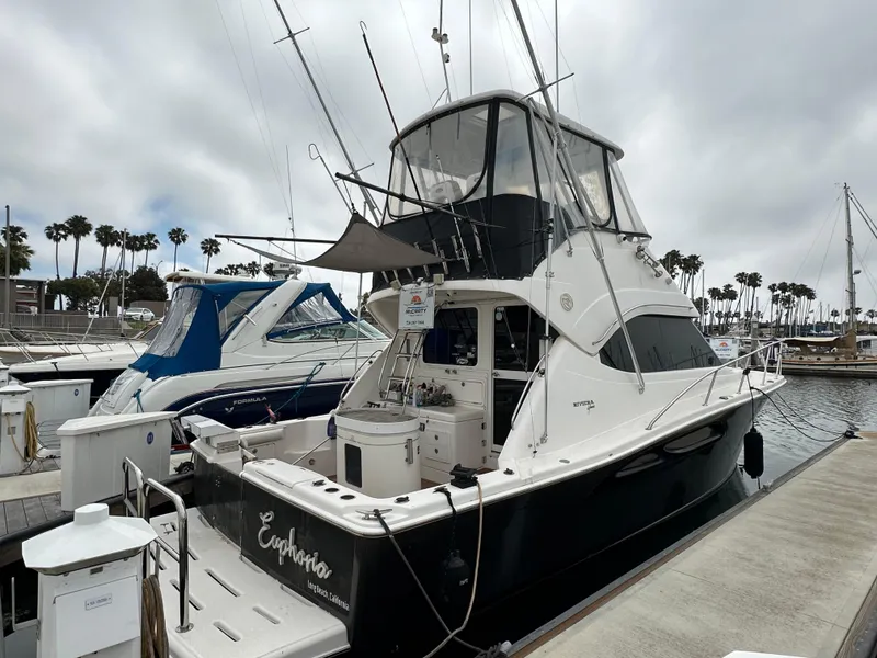 The Image of 2003 Riviera 37 Flybridge yacht docked at marina under cloudy sky. - 0