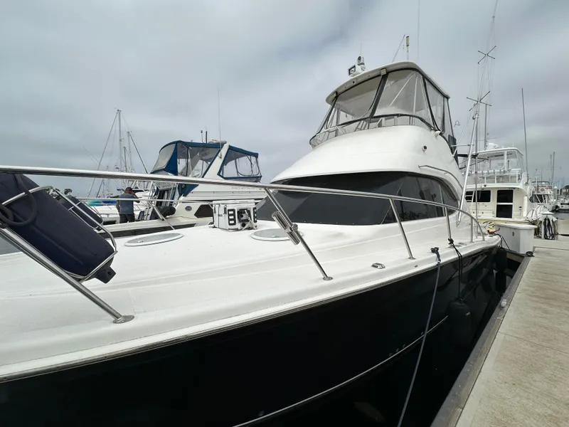 Slide: The Image of 2003 Riviera 37 Flybridge yacht docked at marina under cloudy sky. - 38