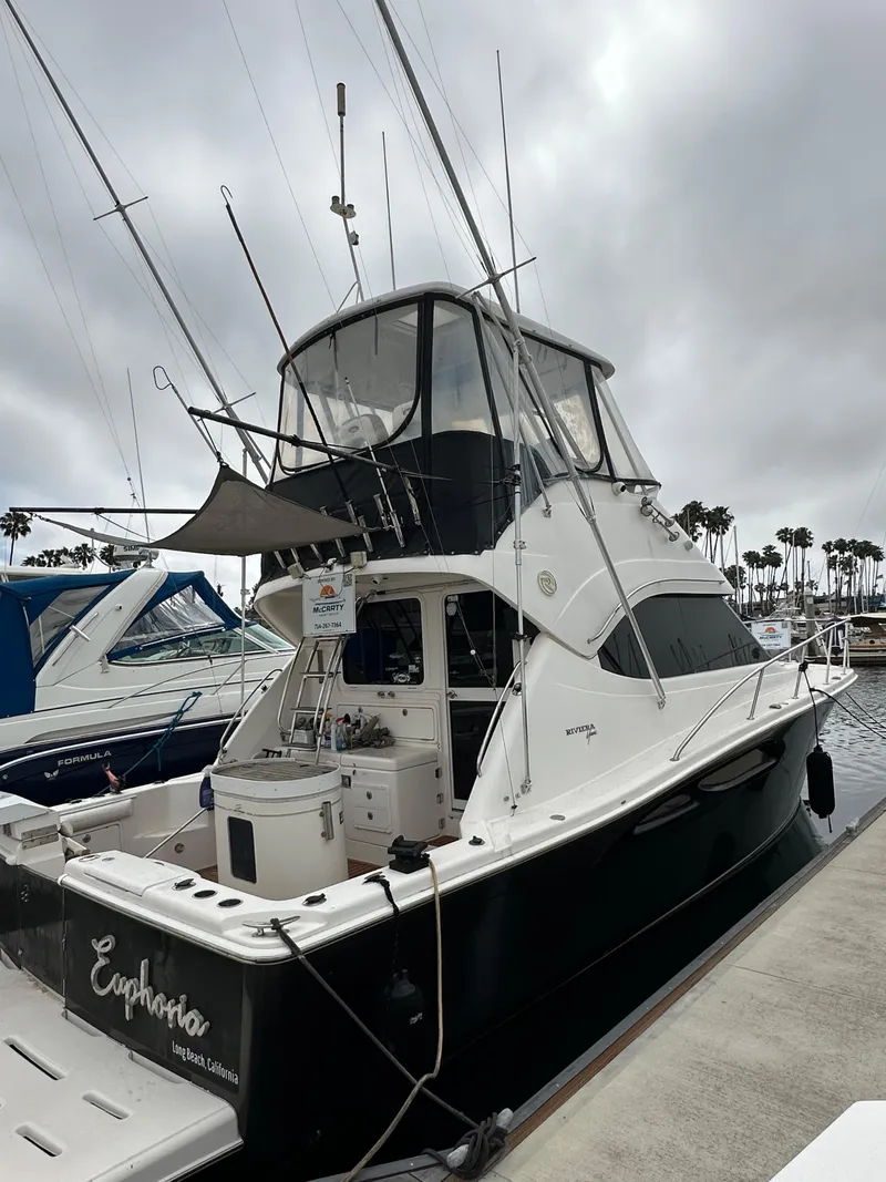 Slide: The Image of 2003 Riviera 37 Flybridge yacht docked at marina under cloudy skies. - 39