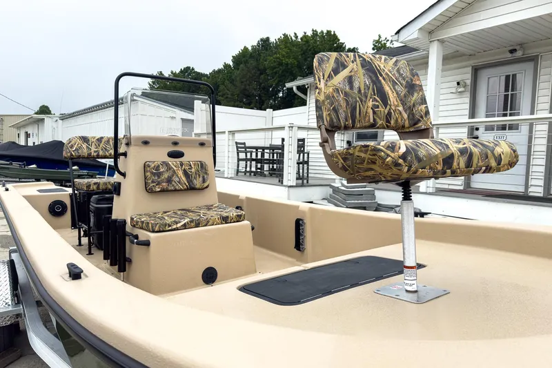 Slide: The Image of 2026 Carolina Skiff E20 JVX CC Sportsman boat with camo seats, docked near a white building. - 2