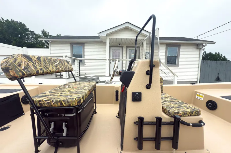 Slide: The Image of 2026 Carolina Skiff E20 JVX CC Sportsman boat with camo seating, parked near a white house. - 4