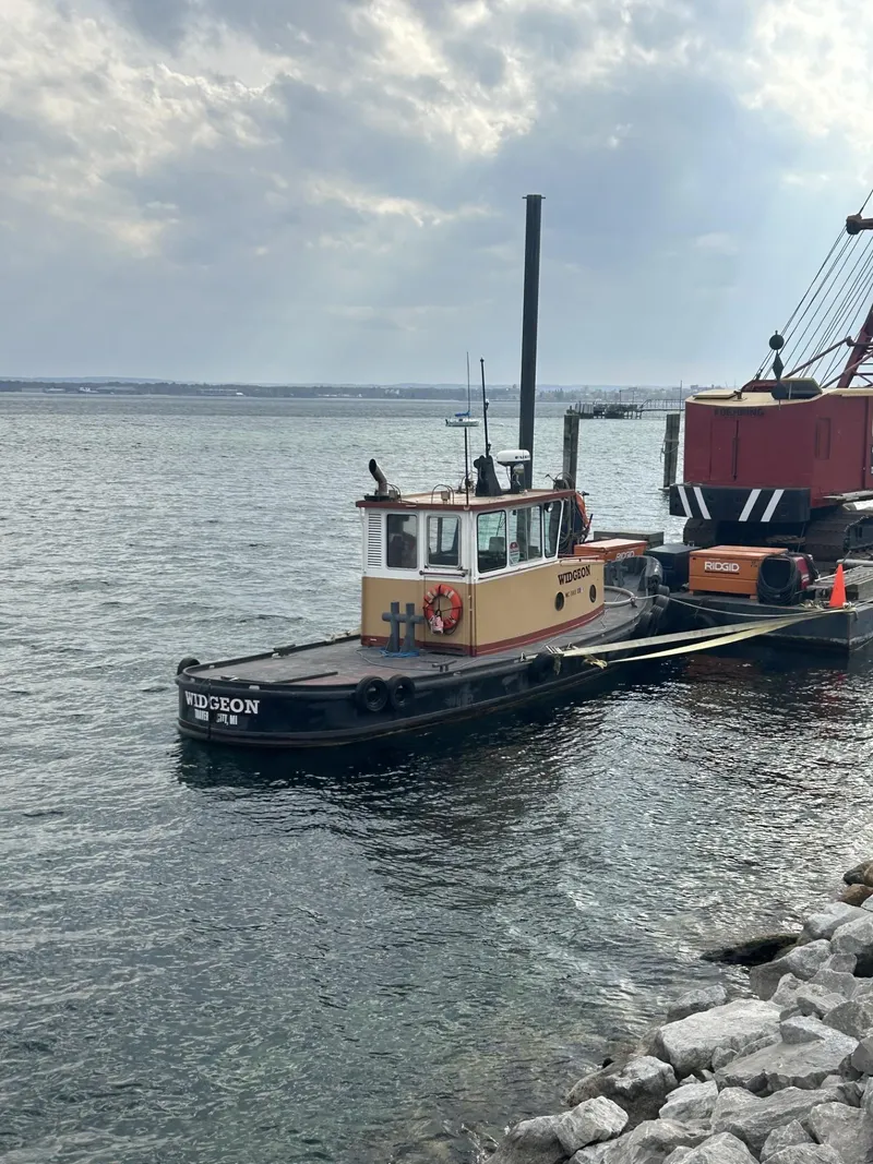 The Image of Vintage 1960 custom commercial tugboat docked by rocky shoreline under cloudy sky. - 1