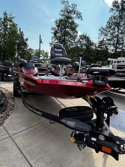 Slide: The Image of 2025 Ranger RT188P boat in showroom, red exterior, parked on trailer, surrounded by trees. - 1