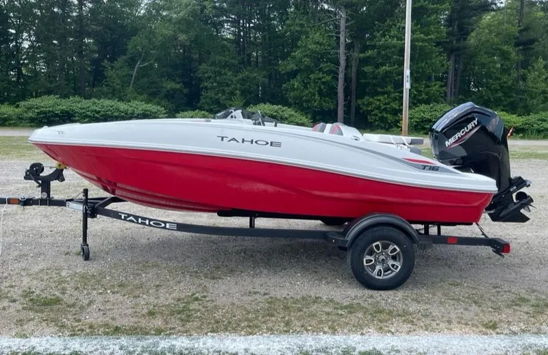 The Image of 2025 Tahoe T16 boat with red and white design on a trailer, parked outdoors. - 0
