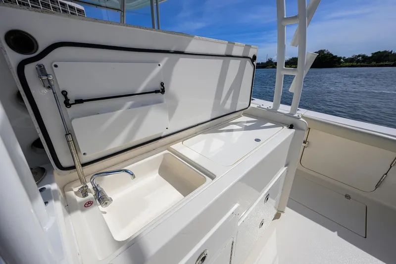 Slide: The Image of 2022 Cobia 350 Center Console boat with open storage compartment and sink, near water. - 21
