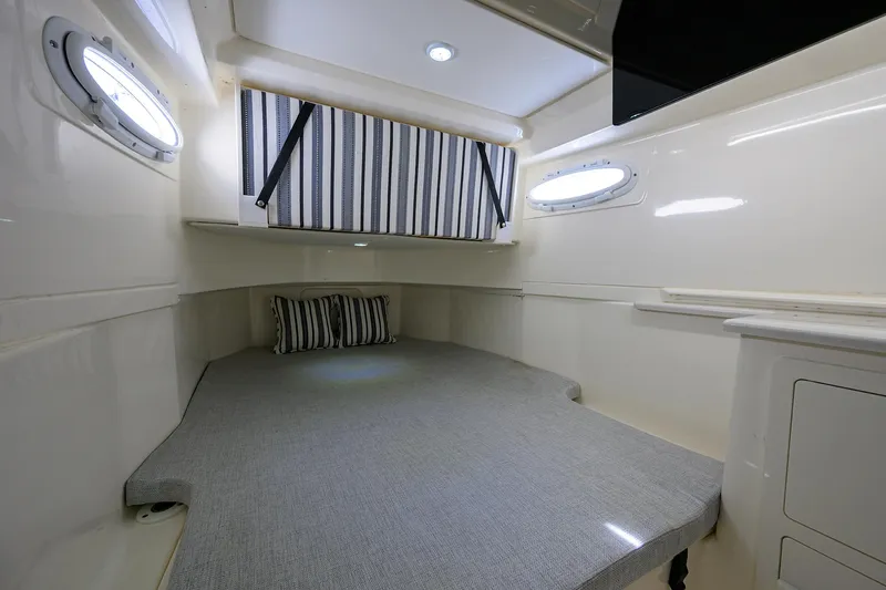 Slide: The Image of 2022 Cobia 350 Center Console cabin interior with bed, striped curtain, and portholes. - 28