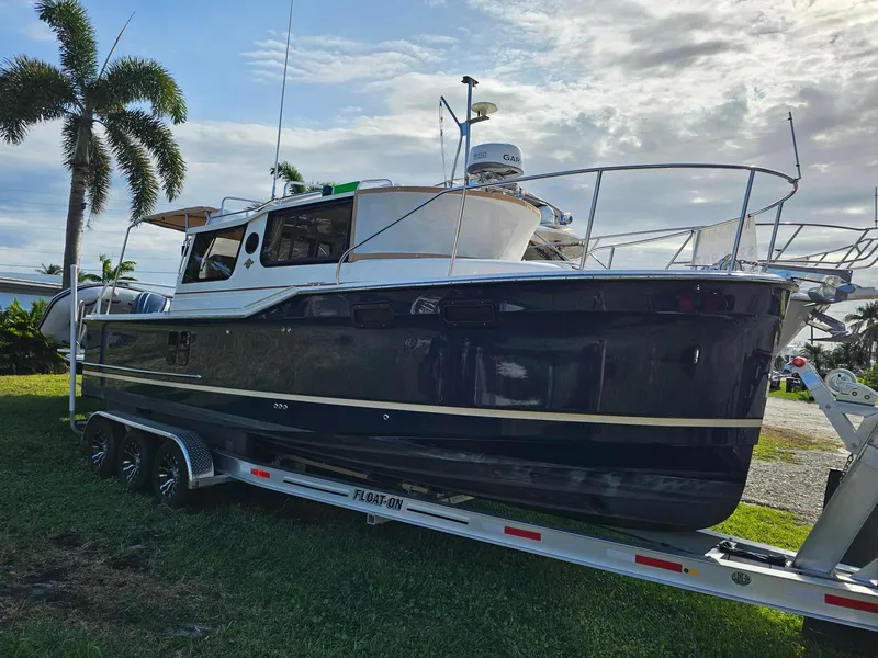 The Image of 2023 Ranger Tugs 27R boat on trailer, parked on grass with palm trees in background. - 0