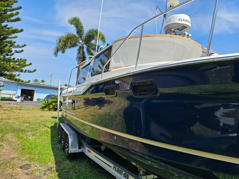 Slide: The Image of 2023 Ranger Tugs 27R boat on trailer, parked on grass with palm trees in background. - 3