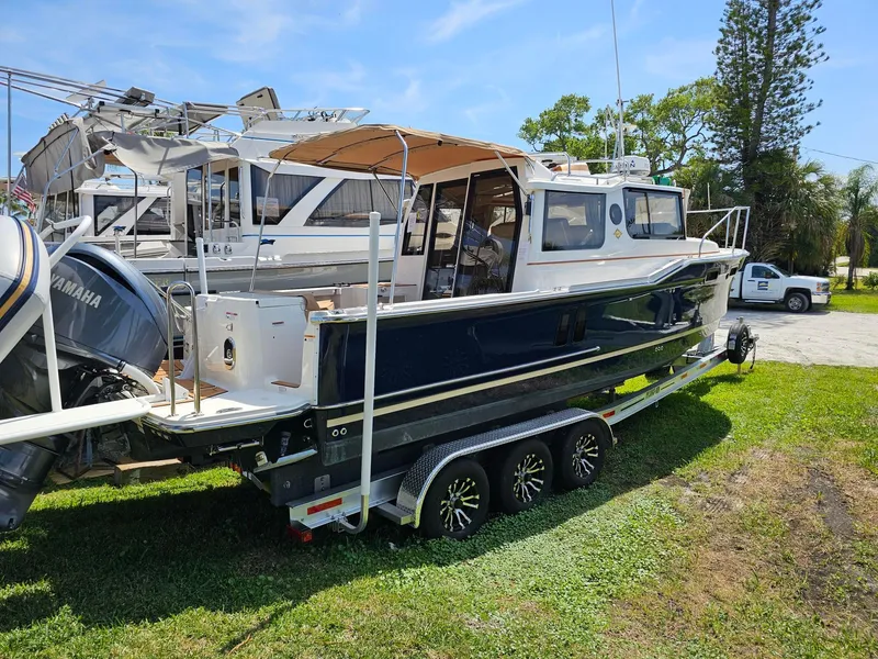 Slide: The Image of 2023 Ranger Tugs 27R boat on trailer, parked on grass, with other boats in background. - 5
