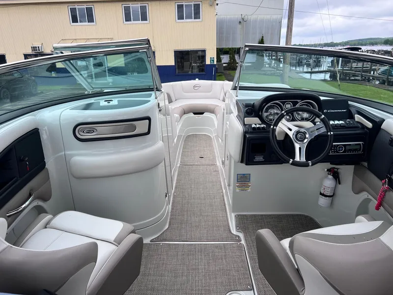 Slide: The Image of 2015 Crownline 285 SS boat interior with steering wheel and seating, docked near buildings. - 7