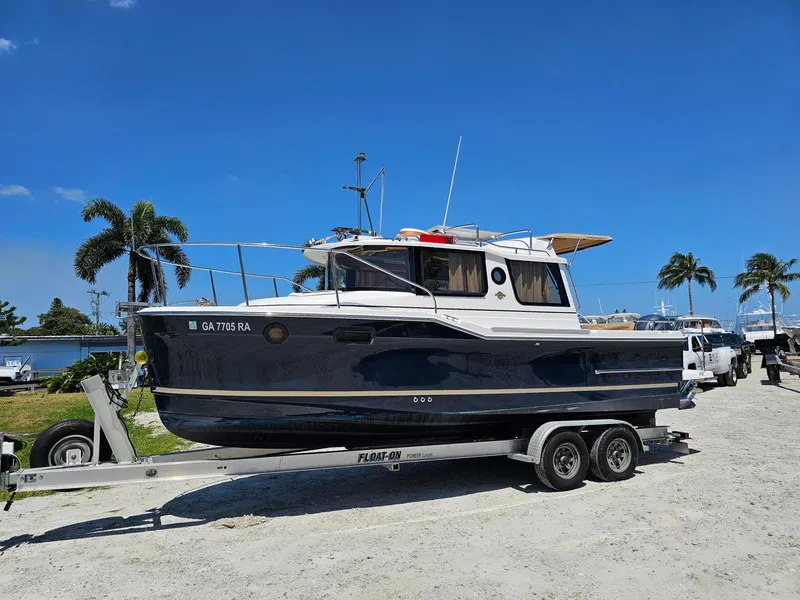 Slide: The Image of 2019 Ranger Tugs 23R boat on trailer, parked near palm trees under clear blue sky. - 7