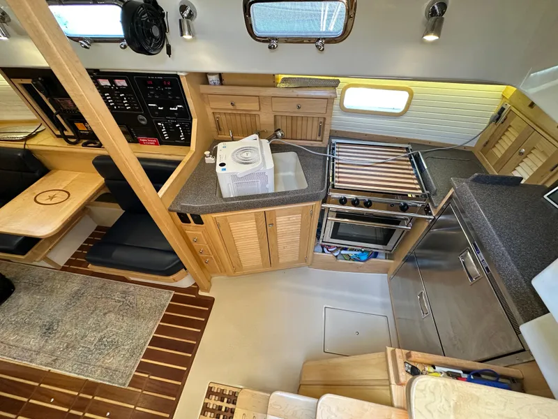 Slide: The Image of Interior of 2021 Island Packet 349 sailboat, featuring a compact kitchen and dining area. - 30
