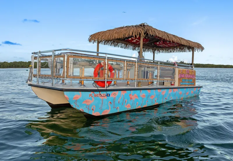 Slide: The Image of 2023 Beachcat 26 Tiki COI boat with tropical design and thatched roof on the water. - 1