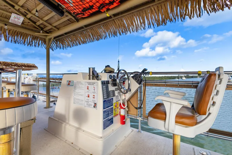 Slide: The Image of Helm of 2023 Beachcat 26 Tiki COI boat with tropical decor and water view. - 11