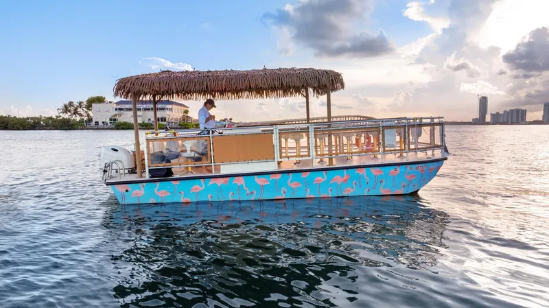 Slide: The Image of 2023 Beachcat 26 Tiki COI boat with flamingo design on calm water at sunset. - 16