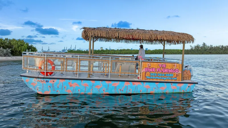 Slide: The Image of 2023 Beachcat 26 Tiki COI boat with flamingo design and thatched roof on water. - 17